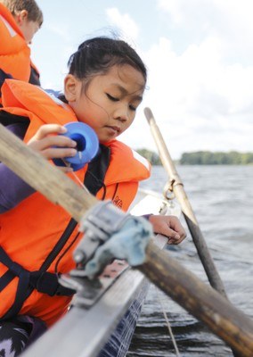Mädchen mit Schwimmweste auf Segelboot hält eine Angelschnur 